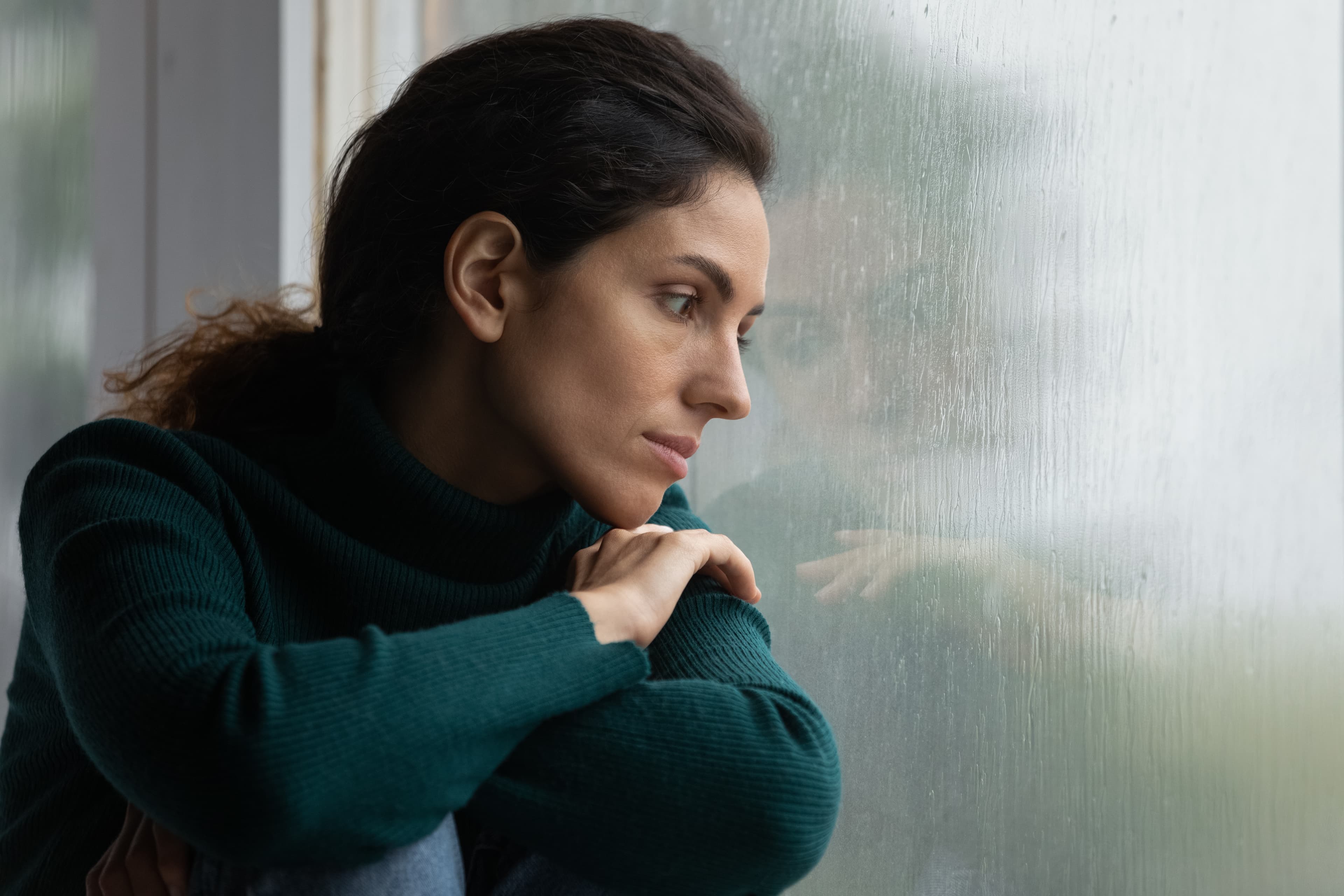 Bild einer Frau, die aus einem Fenster ins den Regen schaut.